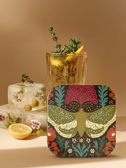 A set of four square hardboard coasters with smoothly rounded corners and a protective high-gloss finish. Each coaster features a unique, highly detailed Art Nouveau style illustration of a moth centered against a dark, botanical background. The intricate artwork uses a rich, moody color palette of deep forest greens, ochre, muted olive, crimson, and black, evoking a vintage, scholarly feel. These decorative drinkware accessories are designed for coffee table and bar cart use.